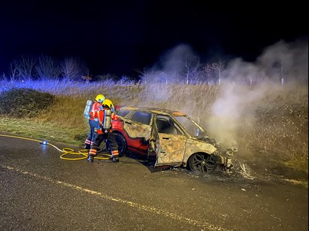 Two firefighters wearing breathing apparatus tackling a car fire.