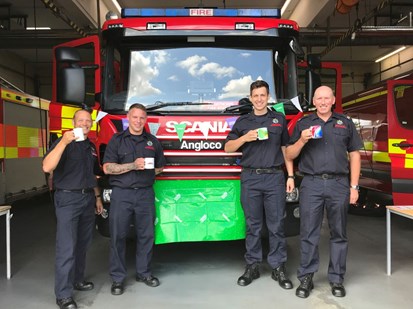 firefighters holding tea cups in front of fire engine