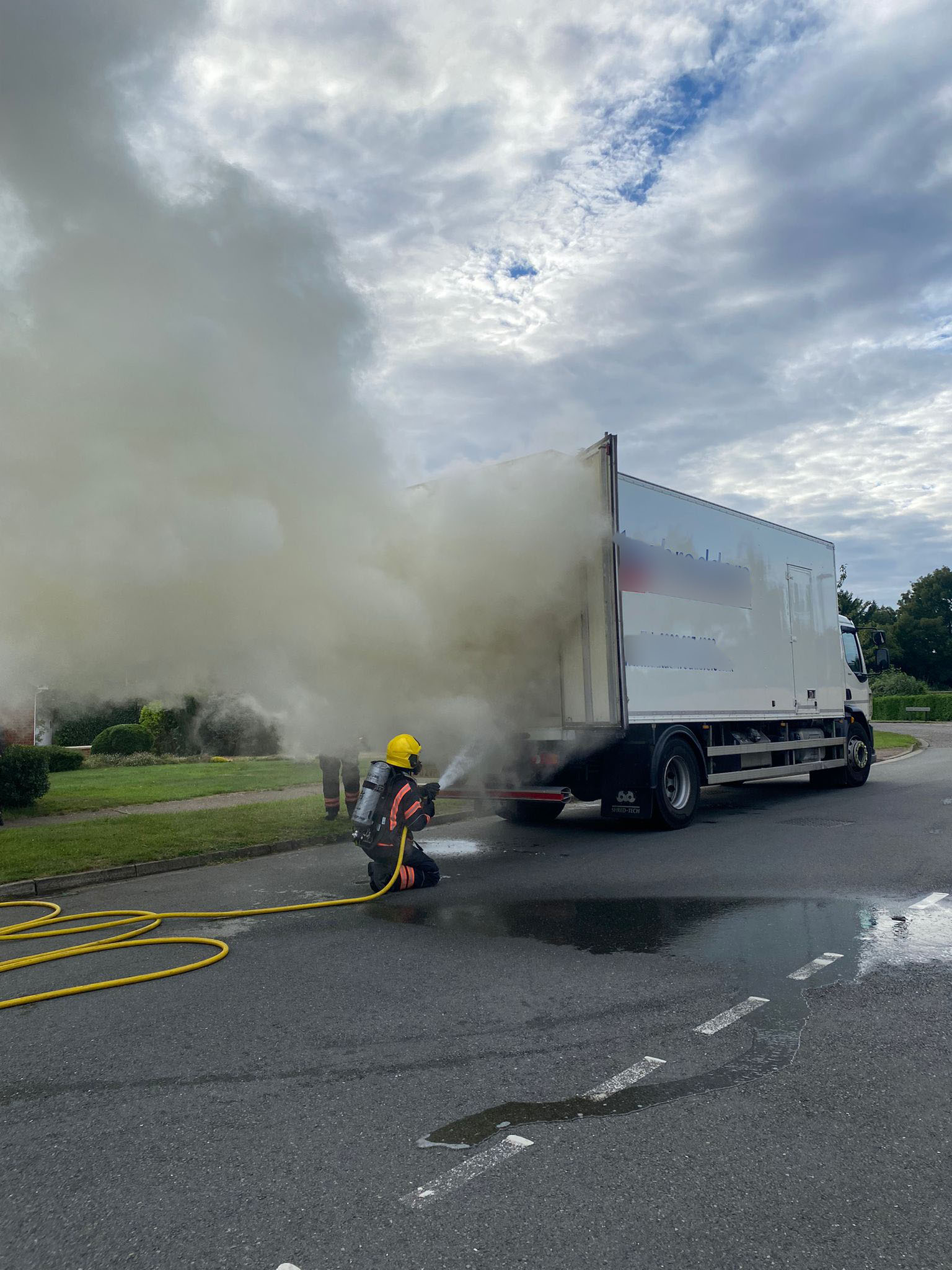 Firefighter wearing breathing apparatus using a hose reel to extinguish a fire in the back of a lorry.