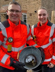 Two firefighters holding a bucket with two ducklings in.